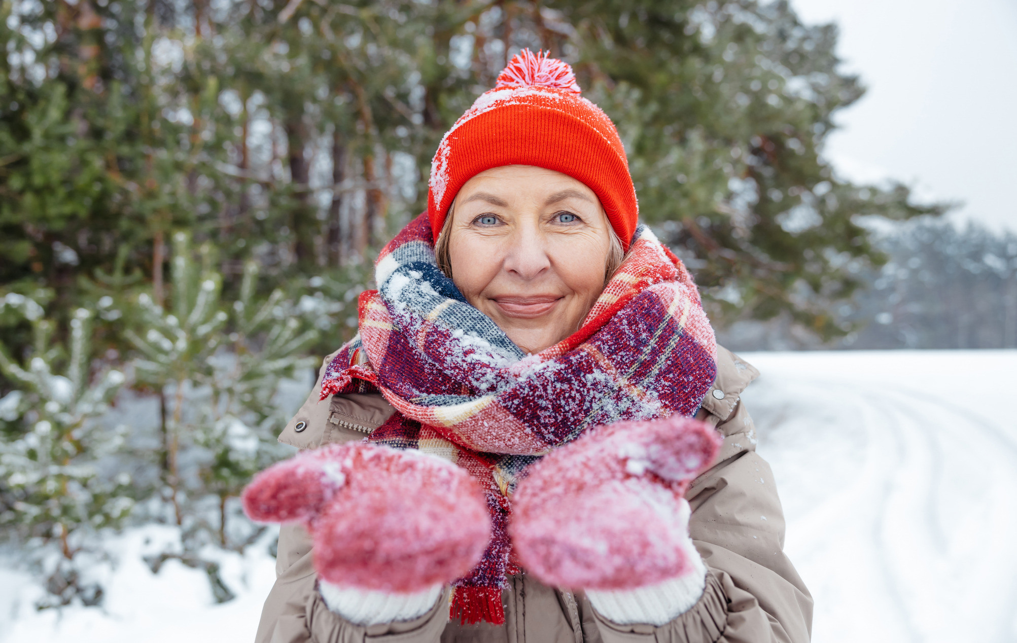 Kvinne i rød lue, votter og skjerf i vintervær viser vottene i vintervær.
