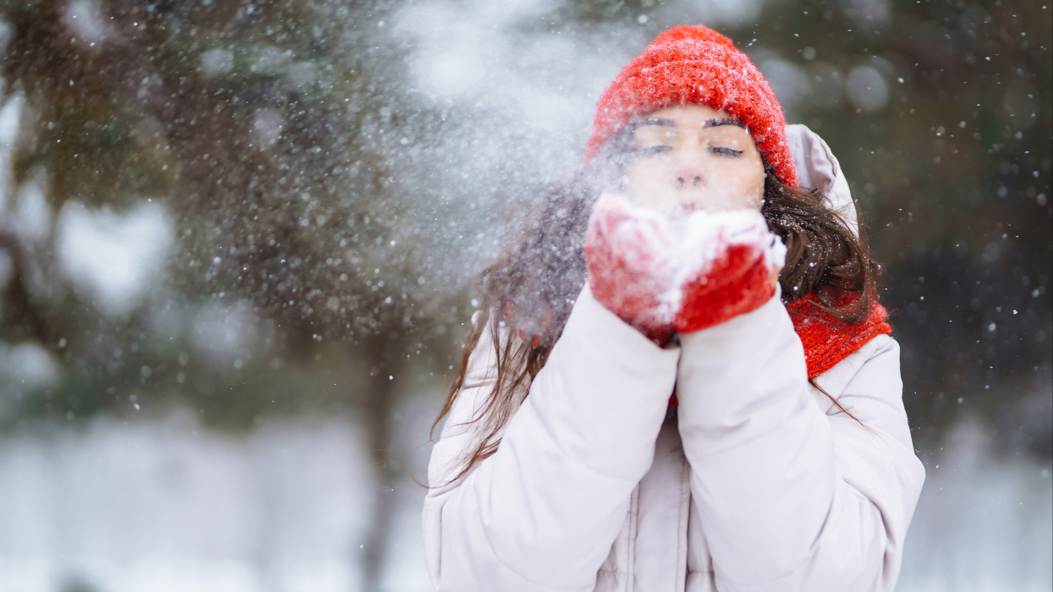 Kvinne i rød lue og rødt skjerf blåser snø mot kamera.