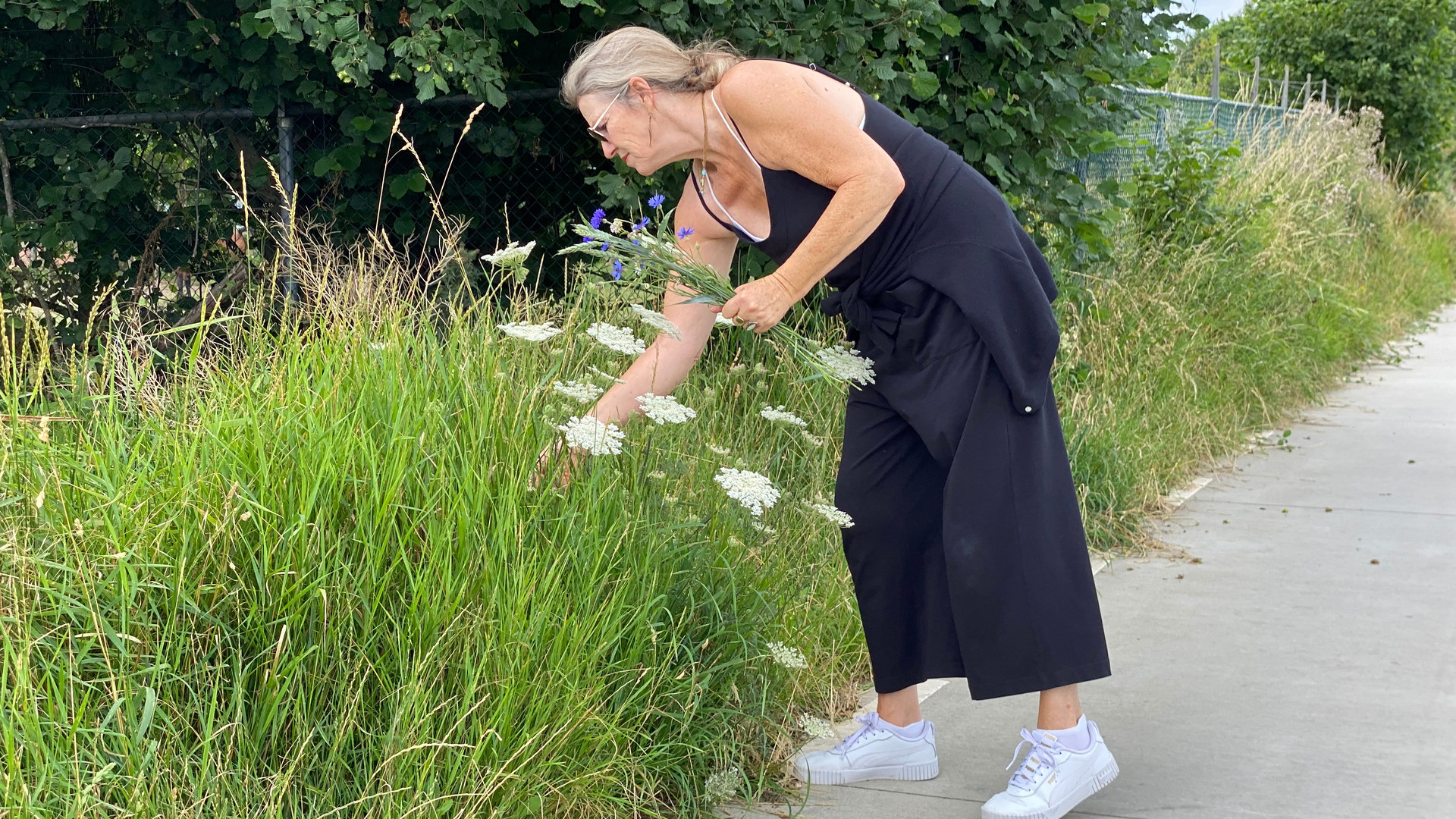 Kvinne står en sommerdag og plukker blomster fra veikanten